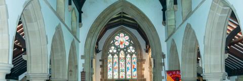 Interior picture of the church feature of the vaulted ceiling, stone arches and the stained glass window