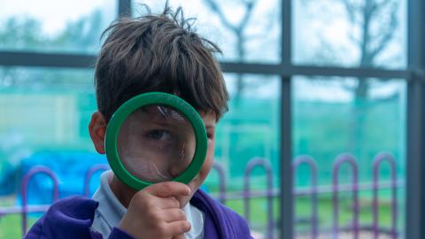 A young boy holds a magnifying glass to his eye