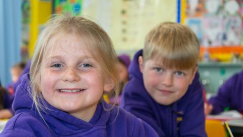 A boy and a girl in in ina classroom smile for the camera