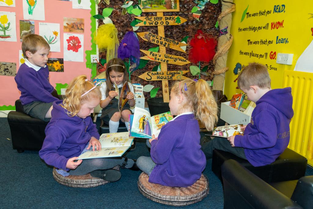 Early years pupil sat on cushions reading picture books