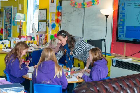 A teacher pointing at a workbook a looked on shared by pupils sat at a desk